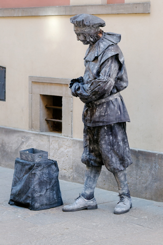 25 - A street performer dressed as a living statue, entirely painted in a metallic silver color